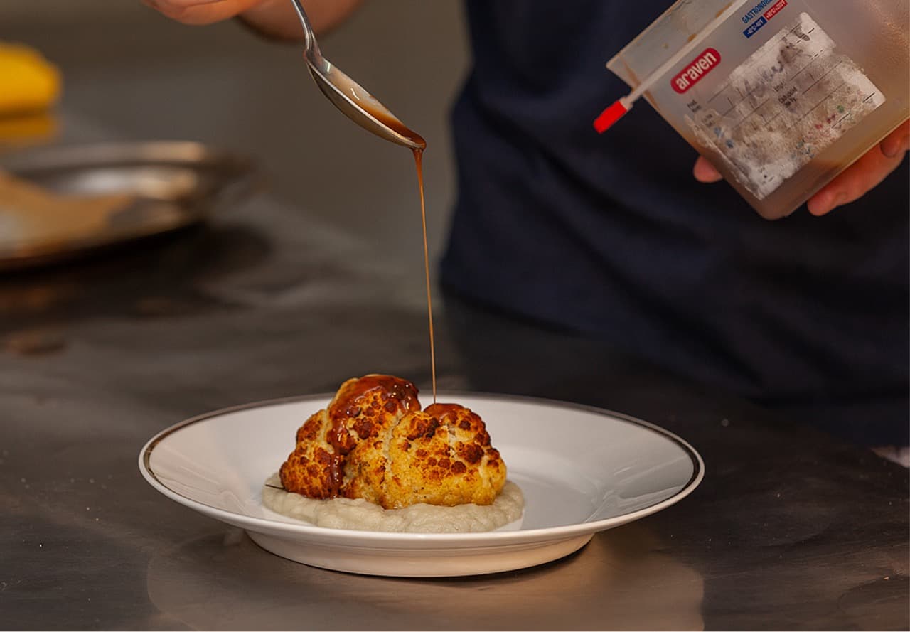 Mani che impiattano una portata in una cucina professionale